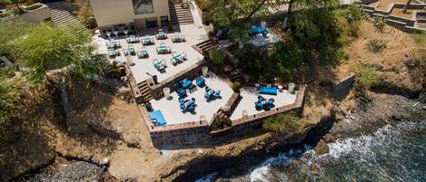 An aerial view of a coastal property with a patio area featuring outdoor seating and a pool.