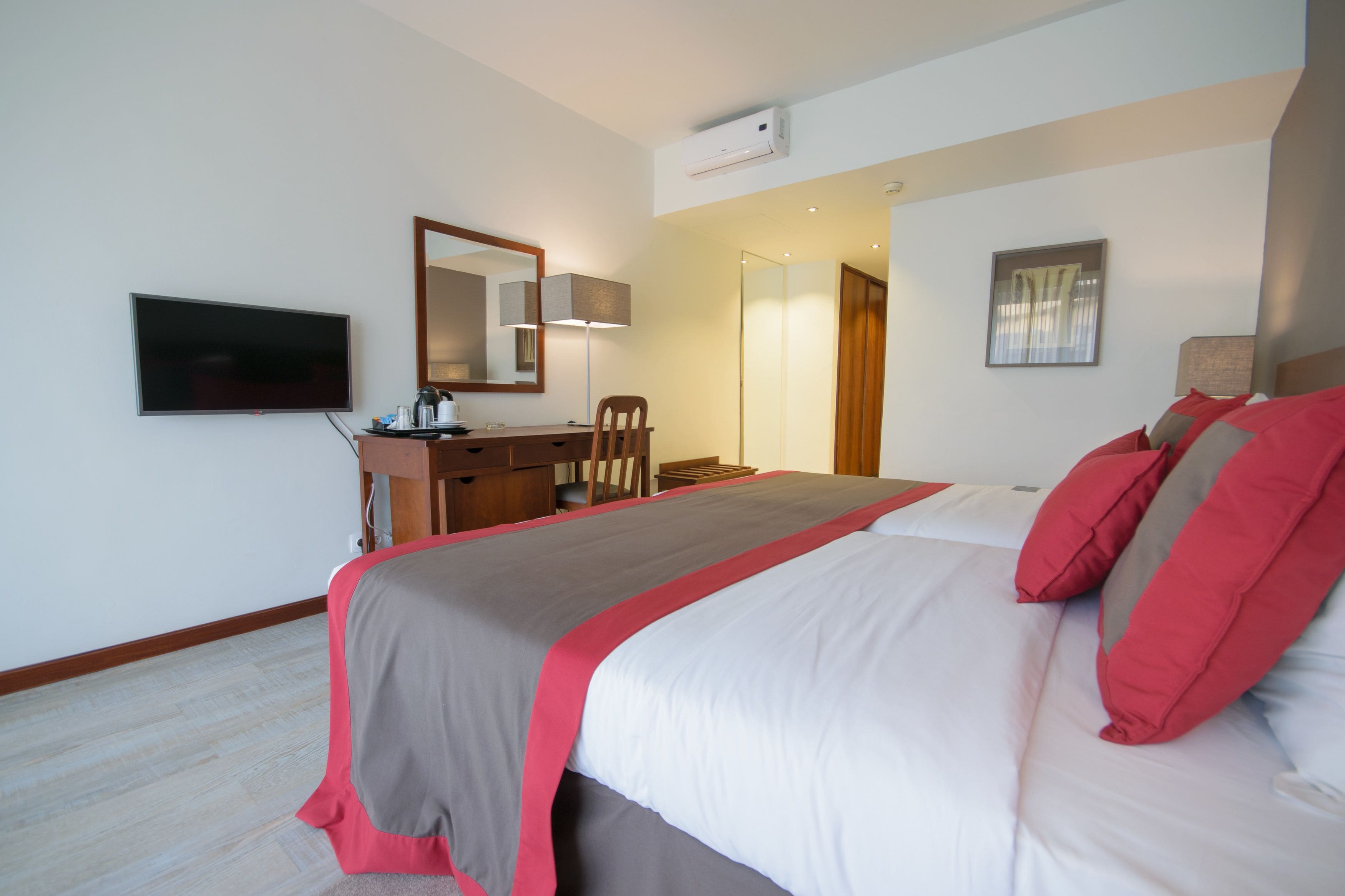 A hotel room with a bed, a desk, a chair, a television, and a mirror.