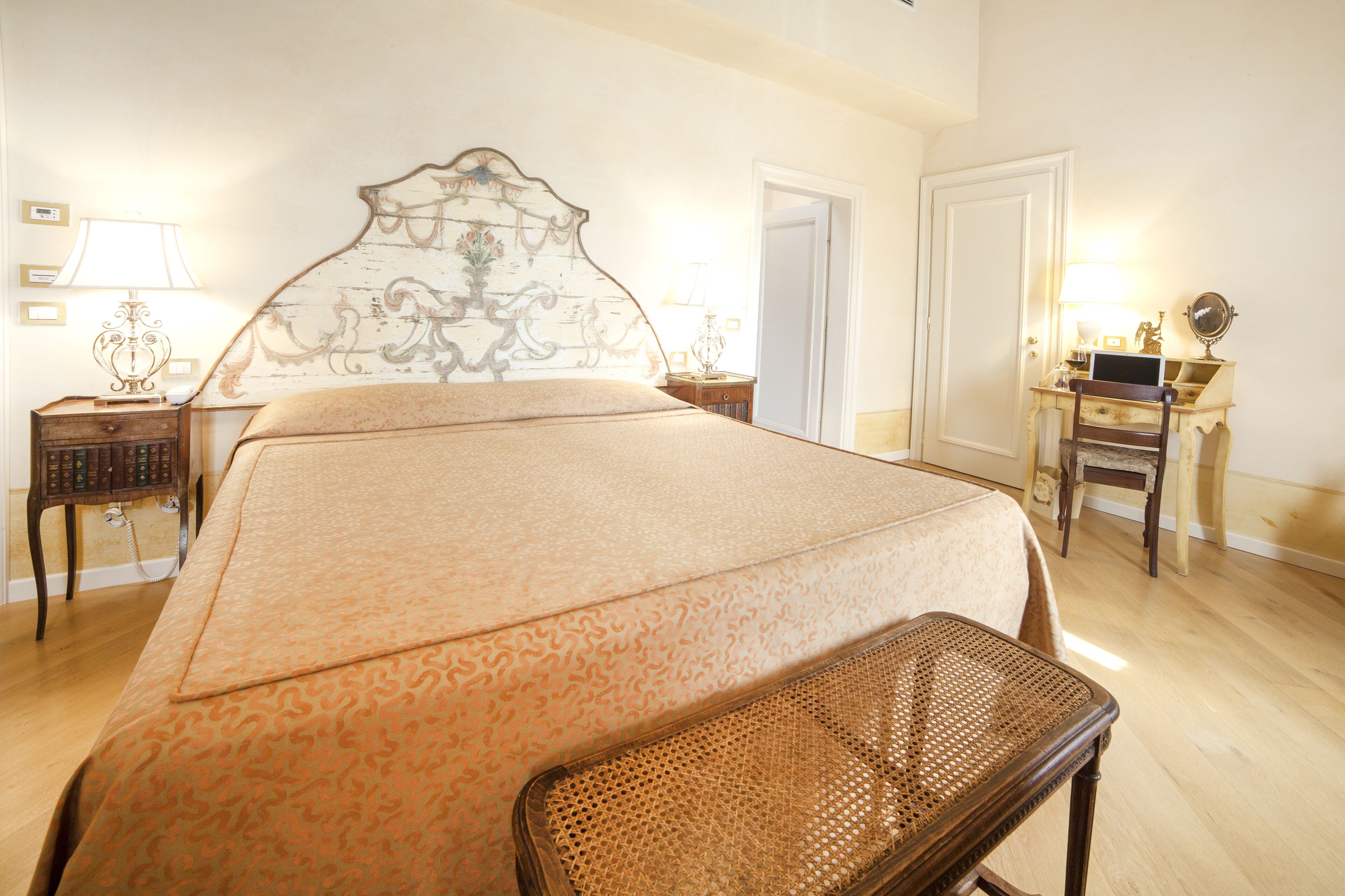 Una camera da letto con un letto grande, un comodino in legno con una lampada, una scrivania con una sedia e una porta.