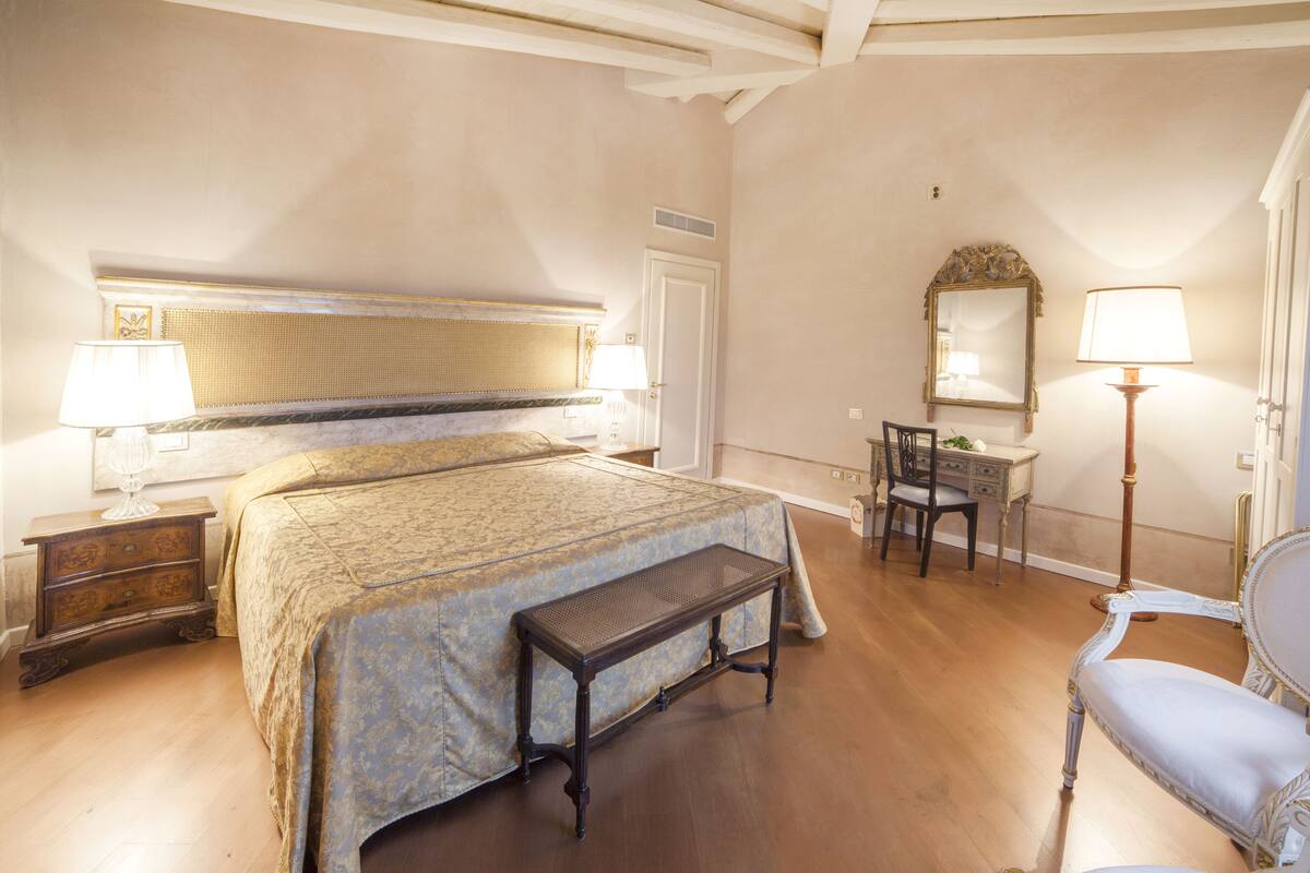 A bedroom with a bed, bedside table, lamp, chair, and a desk with a mirror.