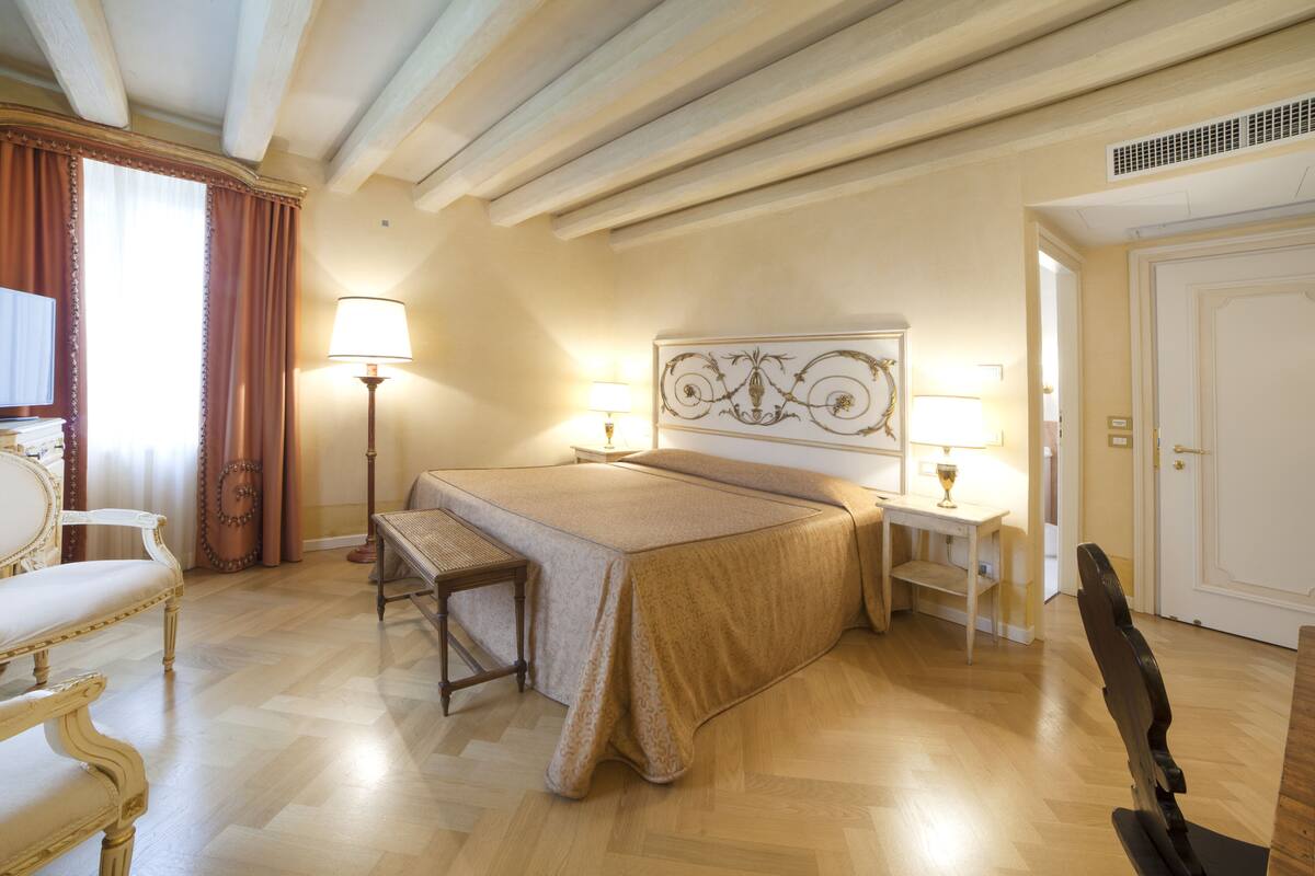 A hotel room with a bed, bedside tables, a lamp, a chair, and a door.