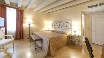 A hotel room with a bed, two bedside tables with lamps, a bench, a chair, and a door.