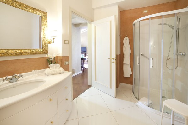 A modern bathroom with a large white sink, gold handles, a gold-framed mirror, a glass-enclosed shower, and a white vanity. - Relais Fra' Lorenzo (Verona)