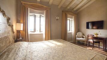A room with a large bed, a desk with a chair, a television, and a window with curtains.