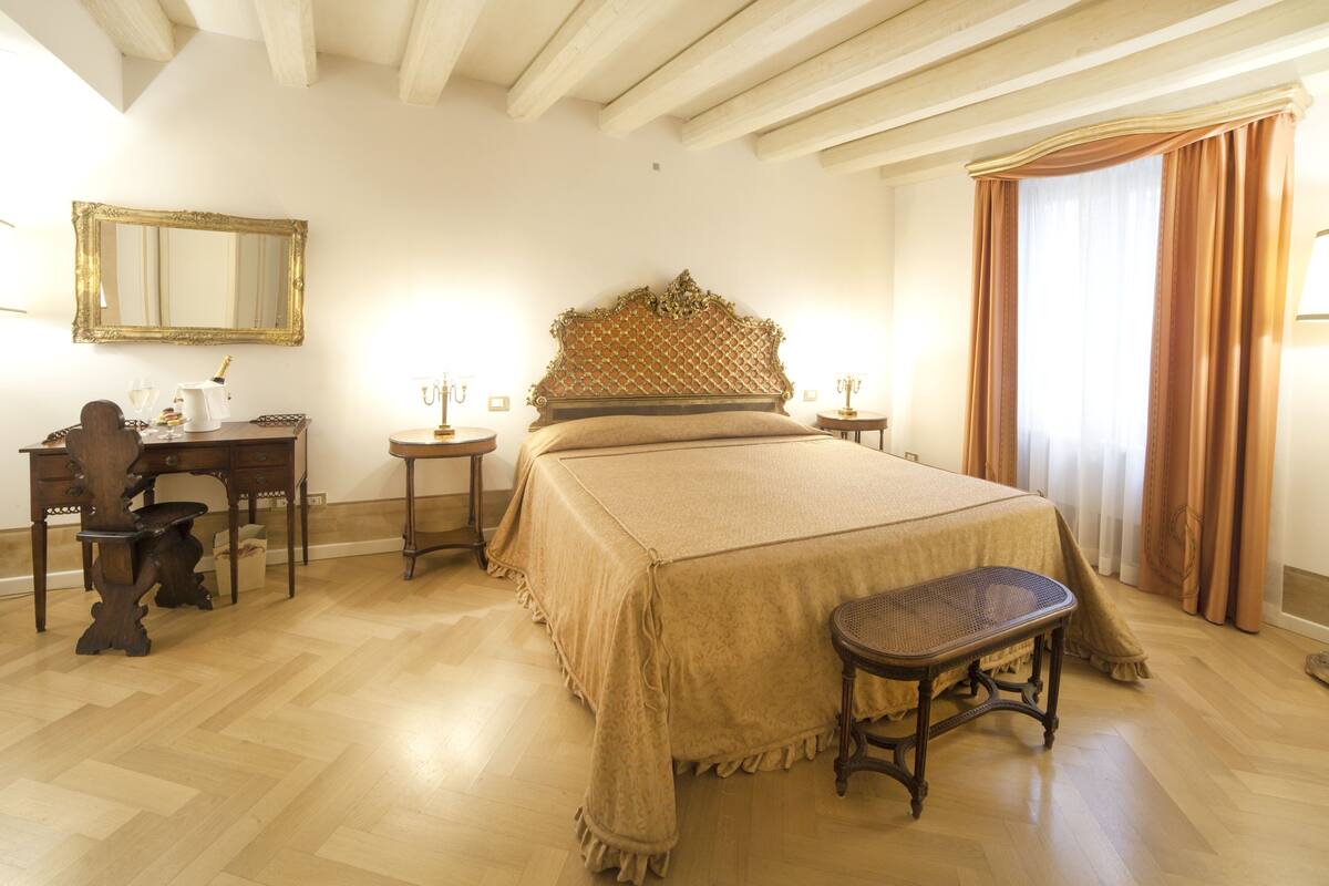 A bedroom with a large bed, a wooden desk, a chair, a mirror, and a window with curtains.