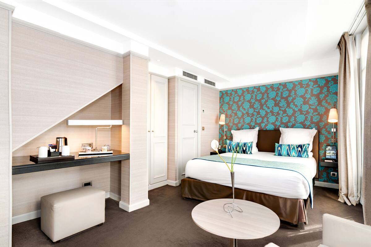 A hotel room with a bed, bedside table, lamp, and a small round table.