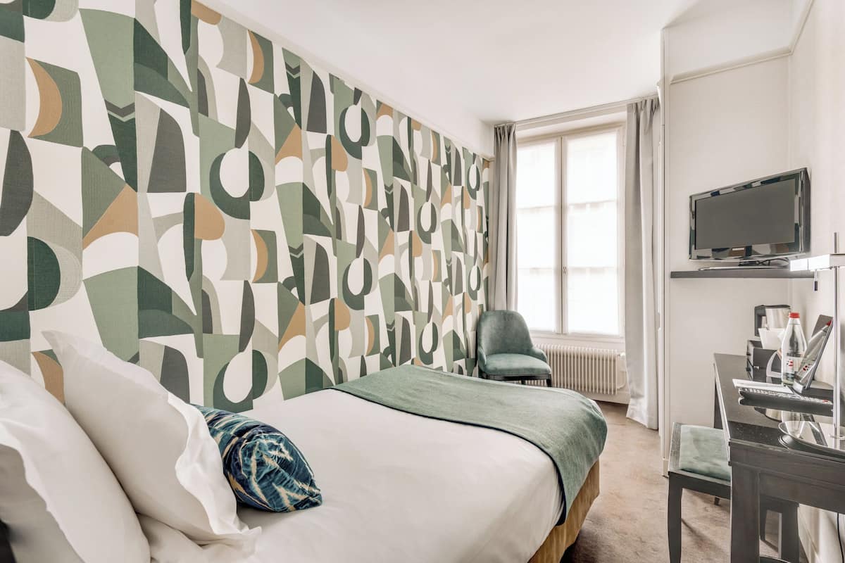 A hotel room with a bed, a desk, a chair, a TV, and a window with curtains.