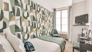 A hotel room with a bed, a desk, a chair, a TV, and a window with curtains.