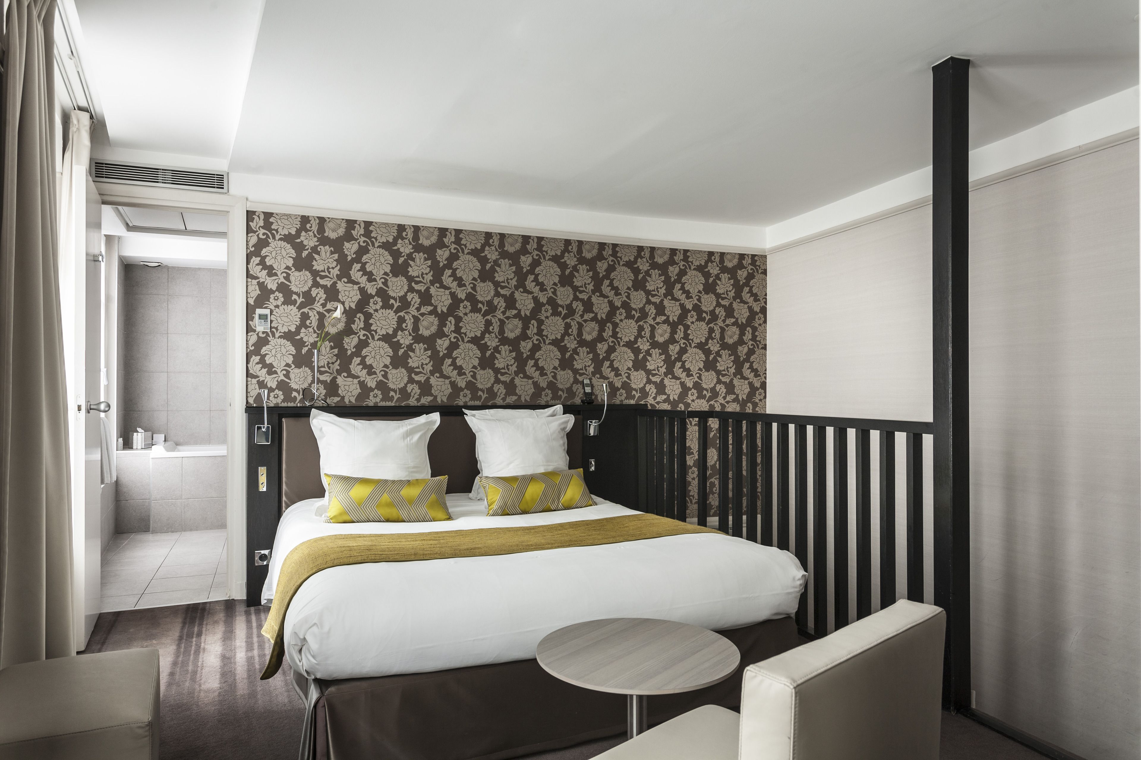 A hotel room with a bed, a round table, a chair, and a bathroom visible through an open door.