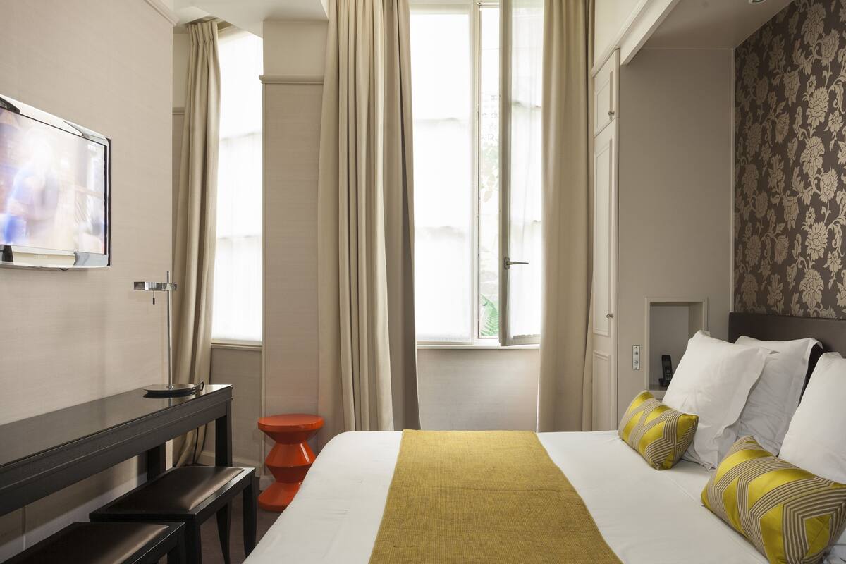 A hotel room with a bed, a desk, a chair, a television, and a window with curtains.
