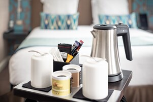 A tray with a coffee maker, a box of coffee pods, a container of tea, and a roll of toilet paper.
