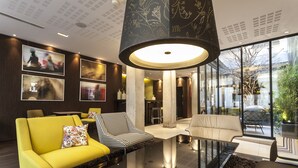 A modern living room with a yellow sofa, a patterned armchair, and a glass coffee table. - Hotel Duo (Paris)