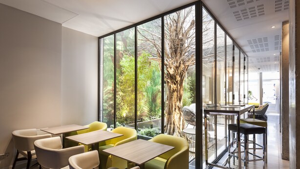 A modern indoor dining area with glass walls, wooden tables, and yellow chairs. - Hotel Duo (Paris)