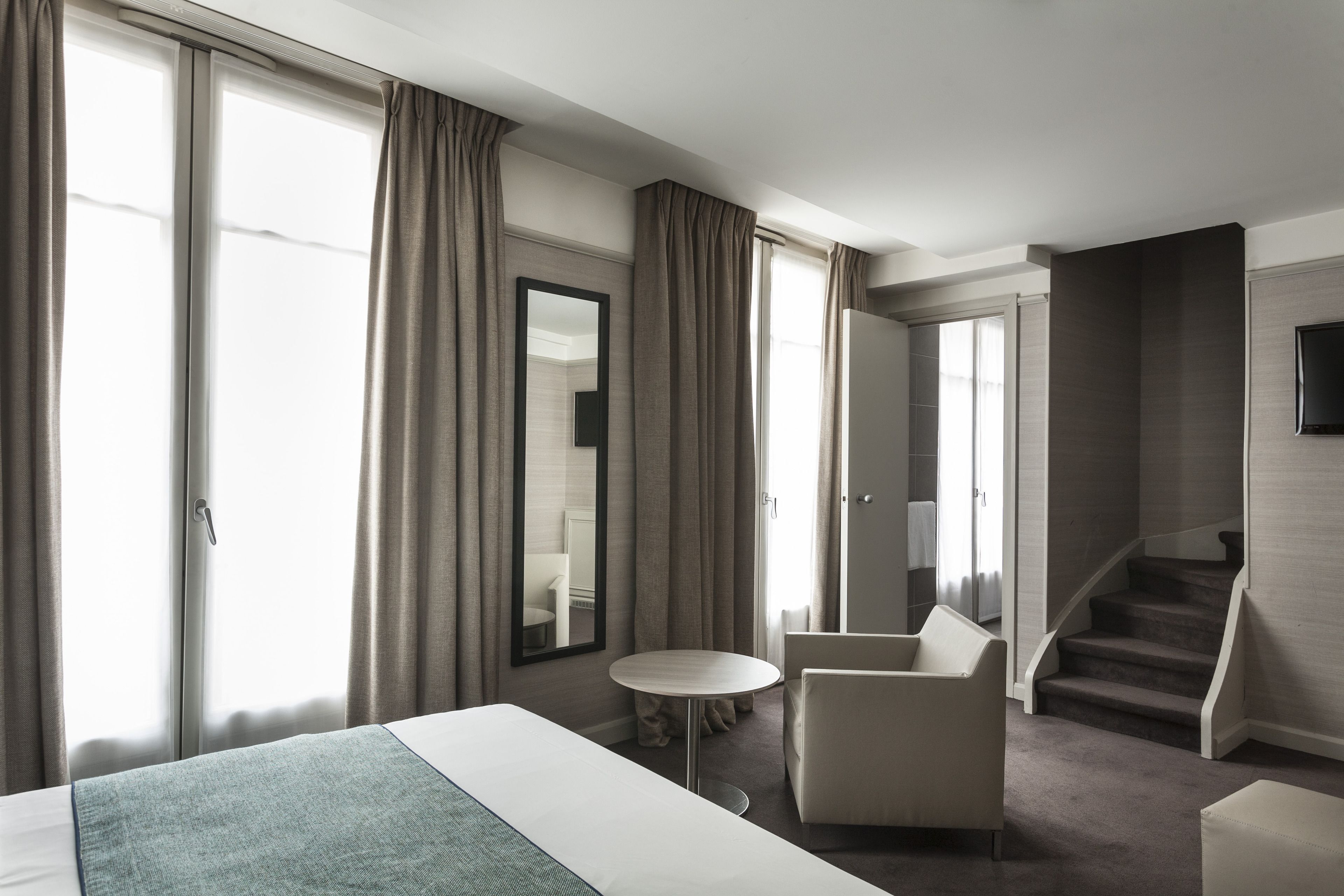 Una habitación de hotel moderna con una cama grande, una mesa redonda, dos sillones, un espejo y una escalera.