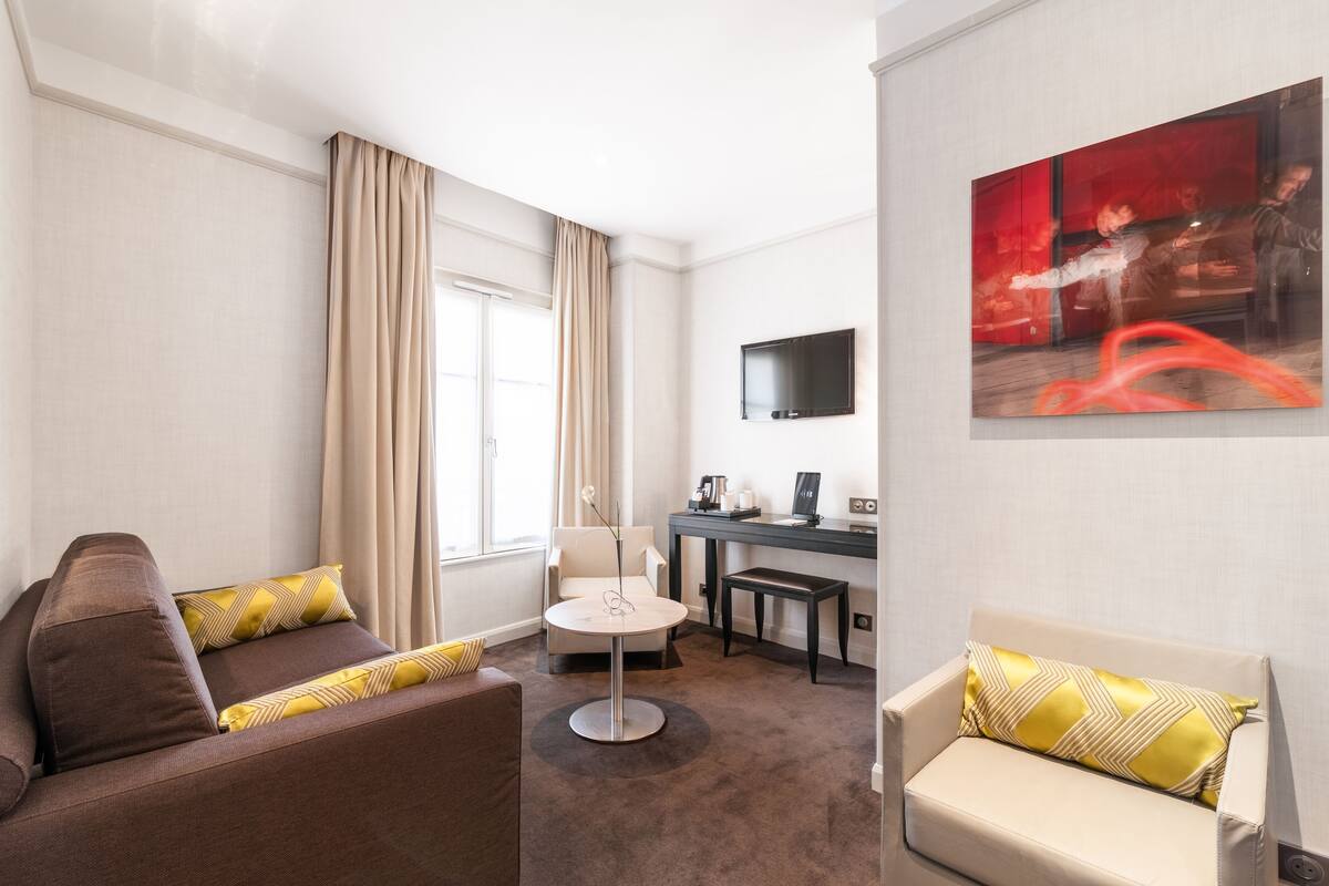A hotel room with a sofa, a small round table, a desk, and a TV mounted on the wall.