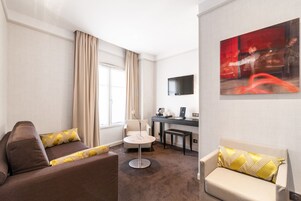 Una habitación de hotel con un sofá, una pequeña mesa redonda, un escritorio y un televisor montado en la pared.