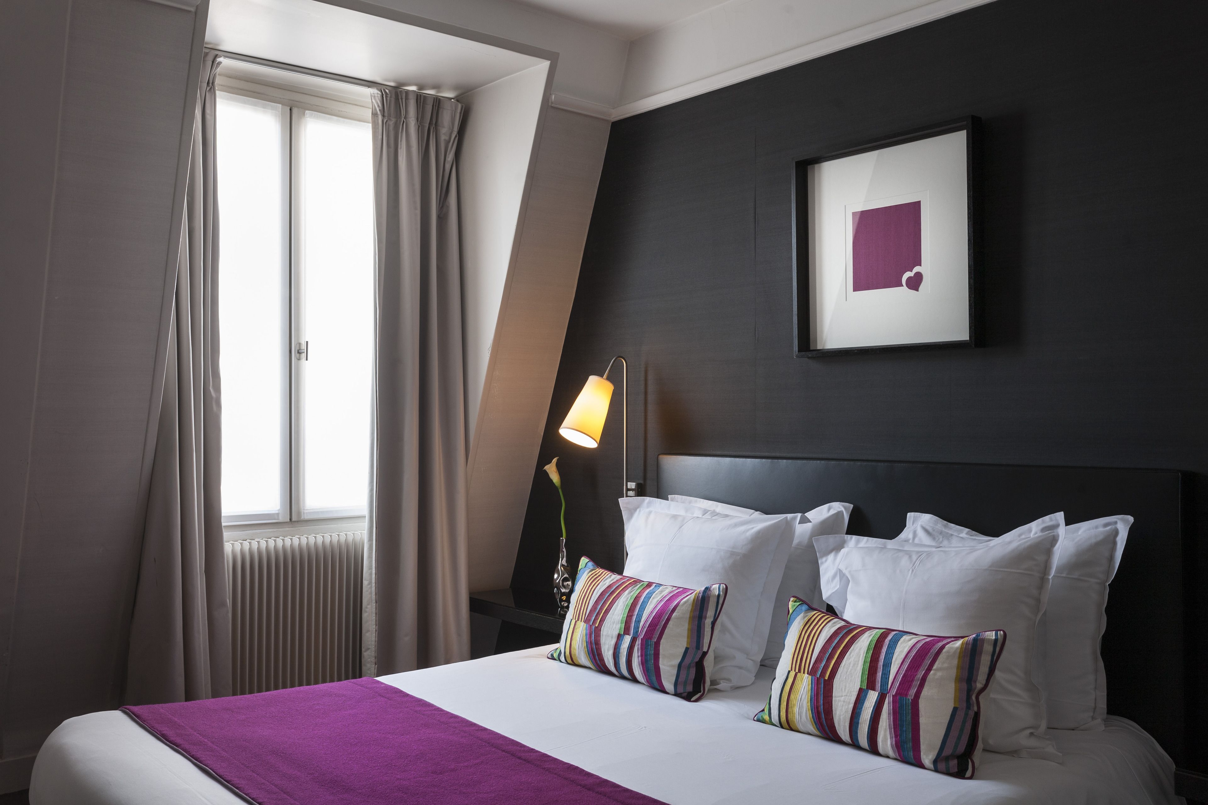 Habitació d'hotel amb un llit, una finestra amb cortines, una làmpada de nit i un quadre al mur.