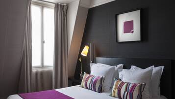 A hotel room with a bed, a window with curtains, a bedside lamp, and a framed picture on the wall.