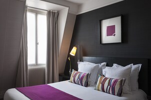 A hotel room with a bed, a window with curtains, a bedside lamp, and a framed picture on the wall.