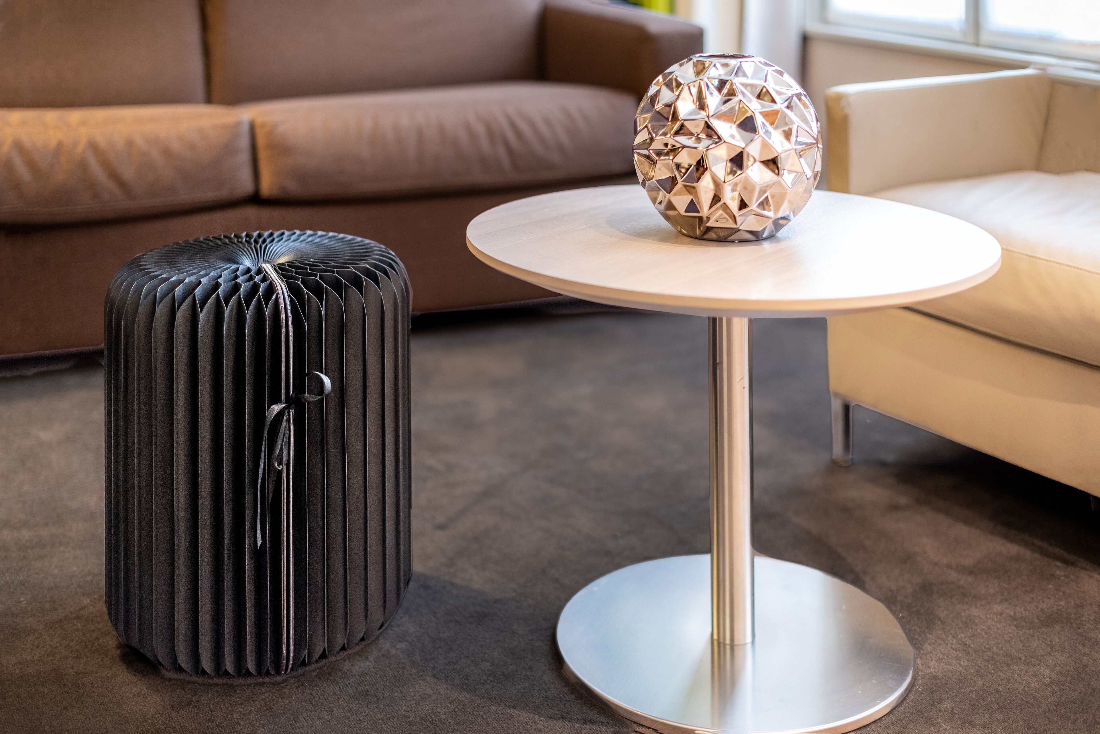 A modern living room with a round table, a decorative metallic sphere, and a black ottoman.