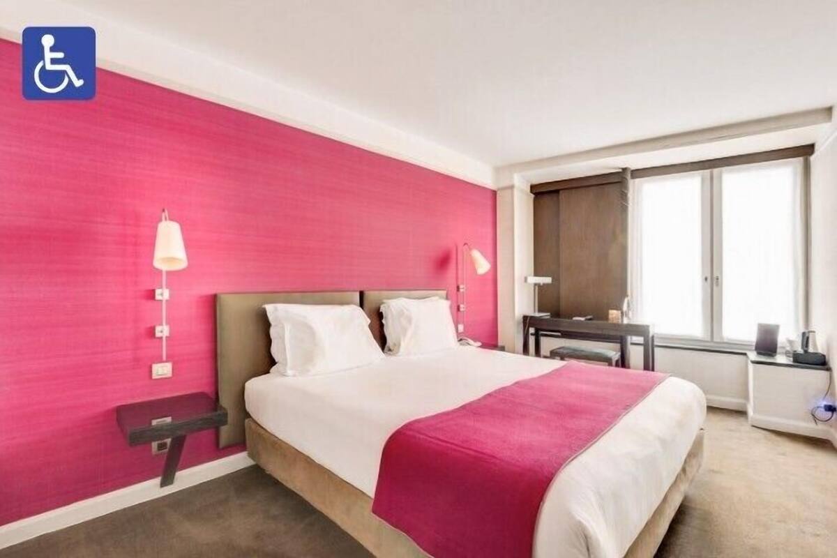 A hotel room with a large bed, a desk, a chair, and a window.