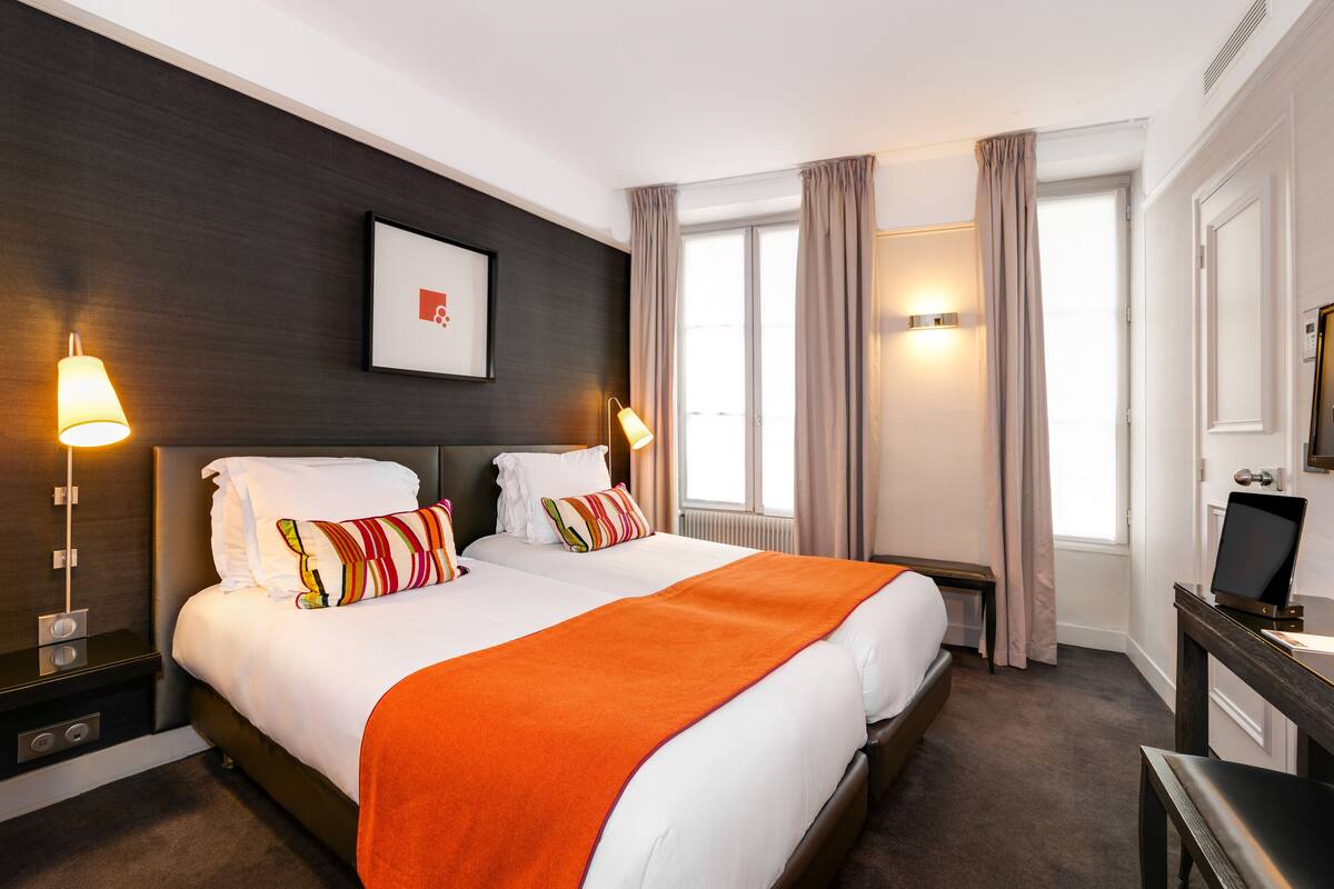 A hotel room with a large bed, two bedside tables, a desk with a chair, a TV, and a window with curtains.