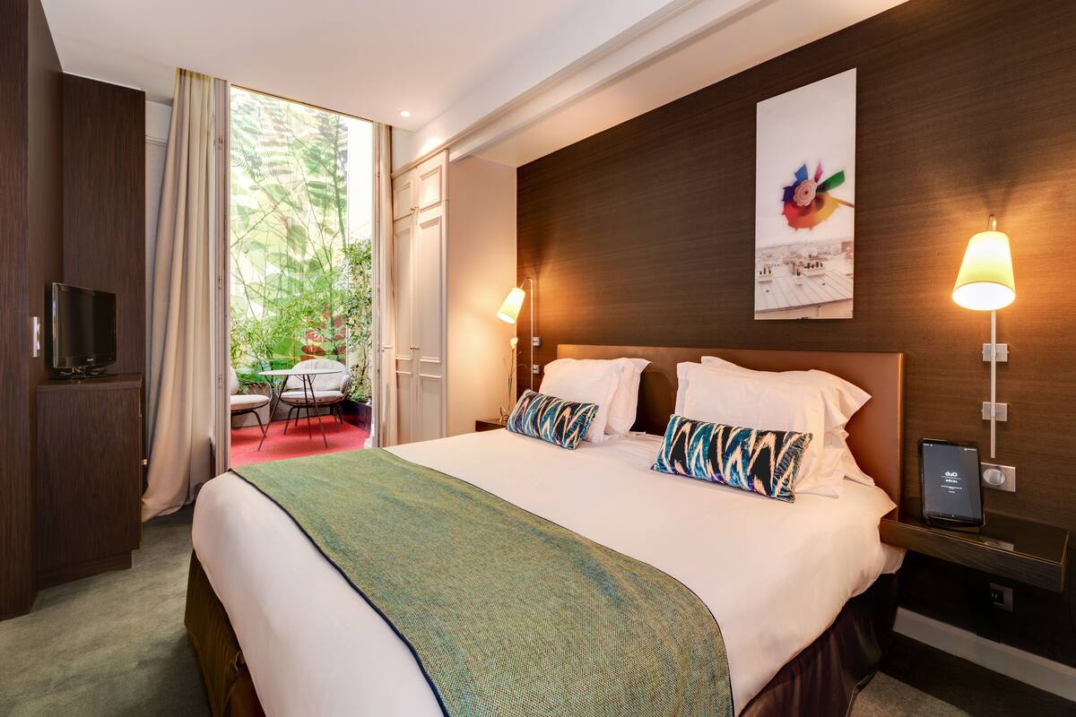 A hotel room with a large bed, a TV, a desk with a chair, and a window with curtains.