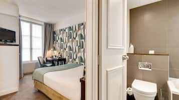 Habitación de hotel con cama, escritorio, silla, televisor y baño con inodoro y lavamanos.