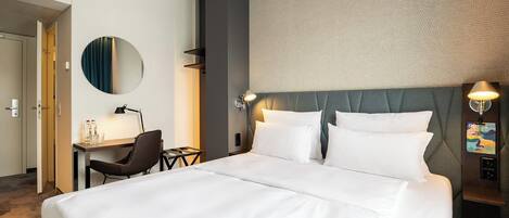 A hotel room with a large bed, a desk, a chair, a round mirror, and a wall with a textured pattern.