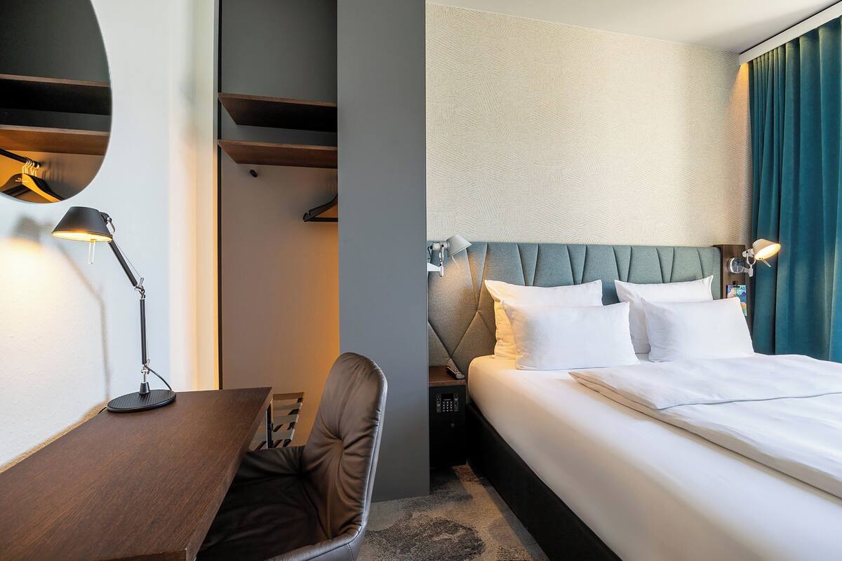 Une chambre d’hôtel comprenant un lit, un bureau, une chaise, une lampe et une armoire.