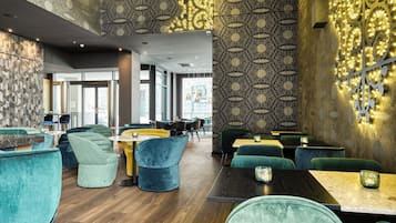 A modern restaurant interior with patterned walls, teal and yellow seating, and a wooden floor.