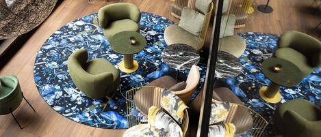 A modern lounge area with green upholstered chairs, round tables, and a central seating area with a patterned floor.