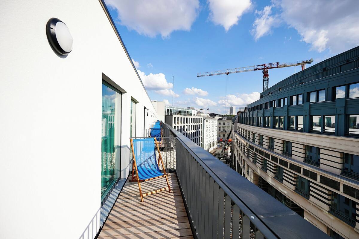 Un balcon avec vue sur une grue de chantier et des immeubles modernes.