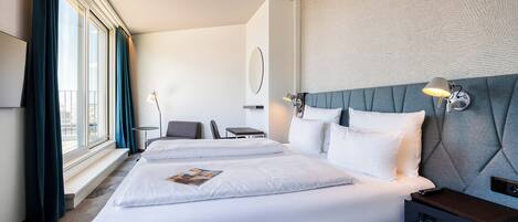 Una habitación de hotel con una cama grande, mesitas de noche, un escritorio y una ventana con cortinas.