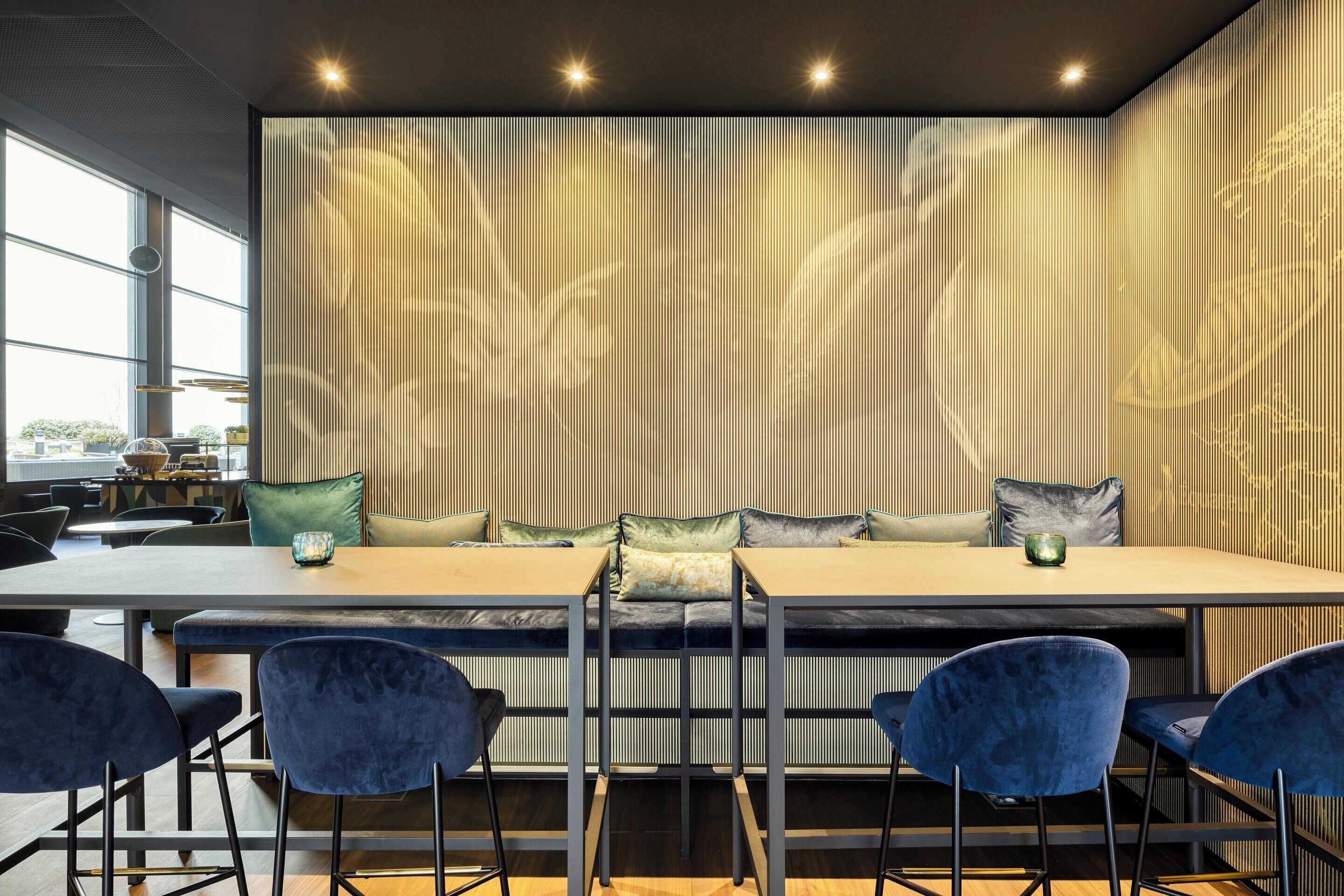 A modern dining area with a long table, blue chairs, and a decorative wall with vertical lines.
