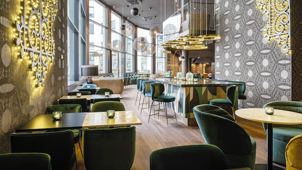 Interior modern d'un restaurant amb cadires tapissades de verd, una zona de bar i parets amb dibuixos.