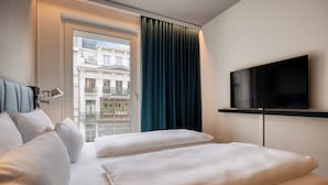 Una habitació d'hotel amb un llit, una televisió, una finestra amb cortines i vista d'un edifici.