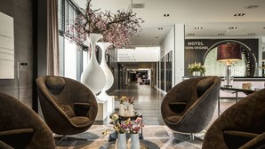 A modern hotel lobby with a reception desk, seating area, and a large decorative vase with flowers. - Van der Valk Hotel Uden-Veghel (Uden)