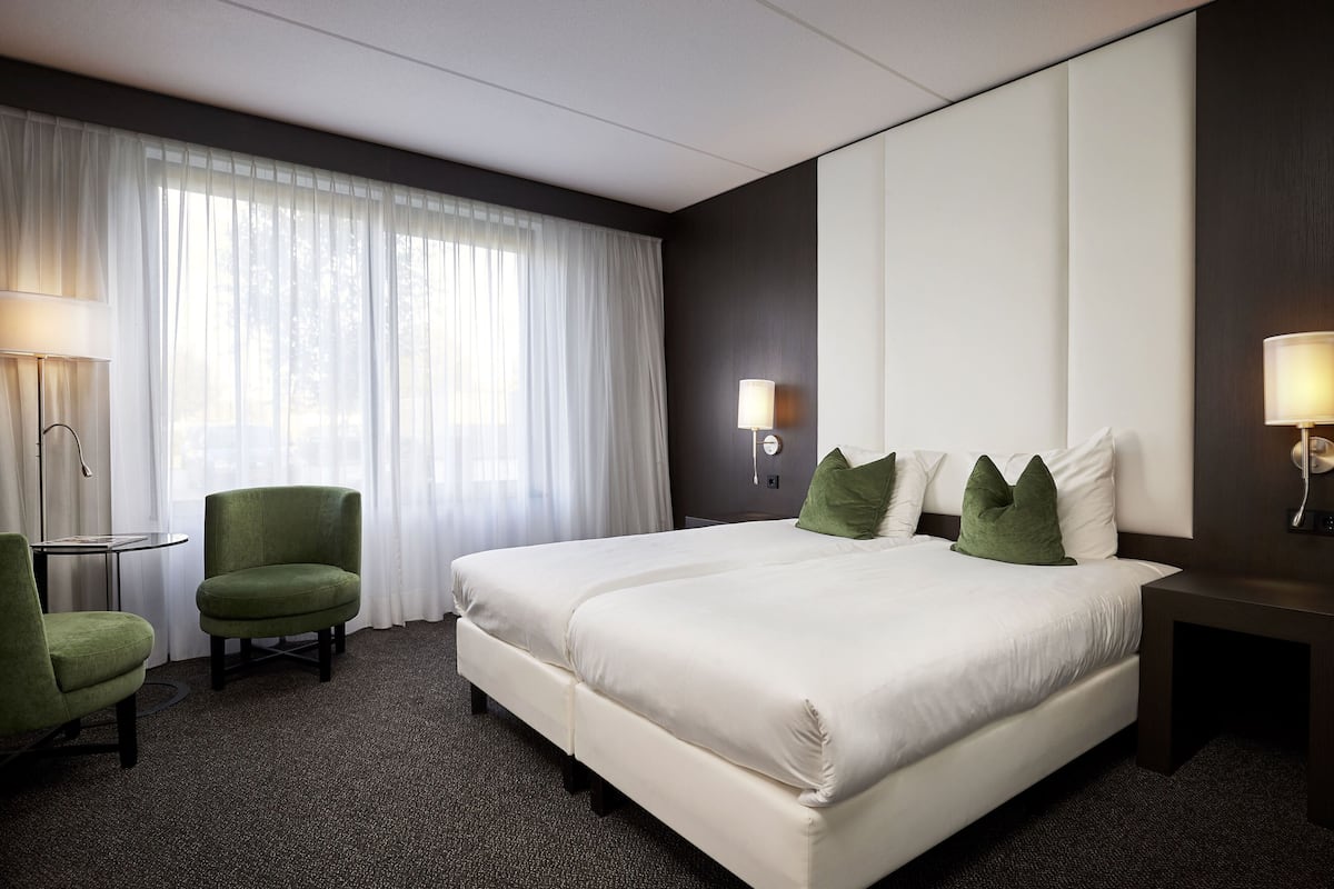 A hotel room with a large bed, two chairs, a small table, and a lamp.