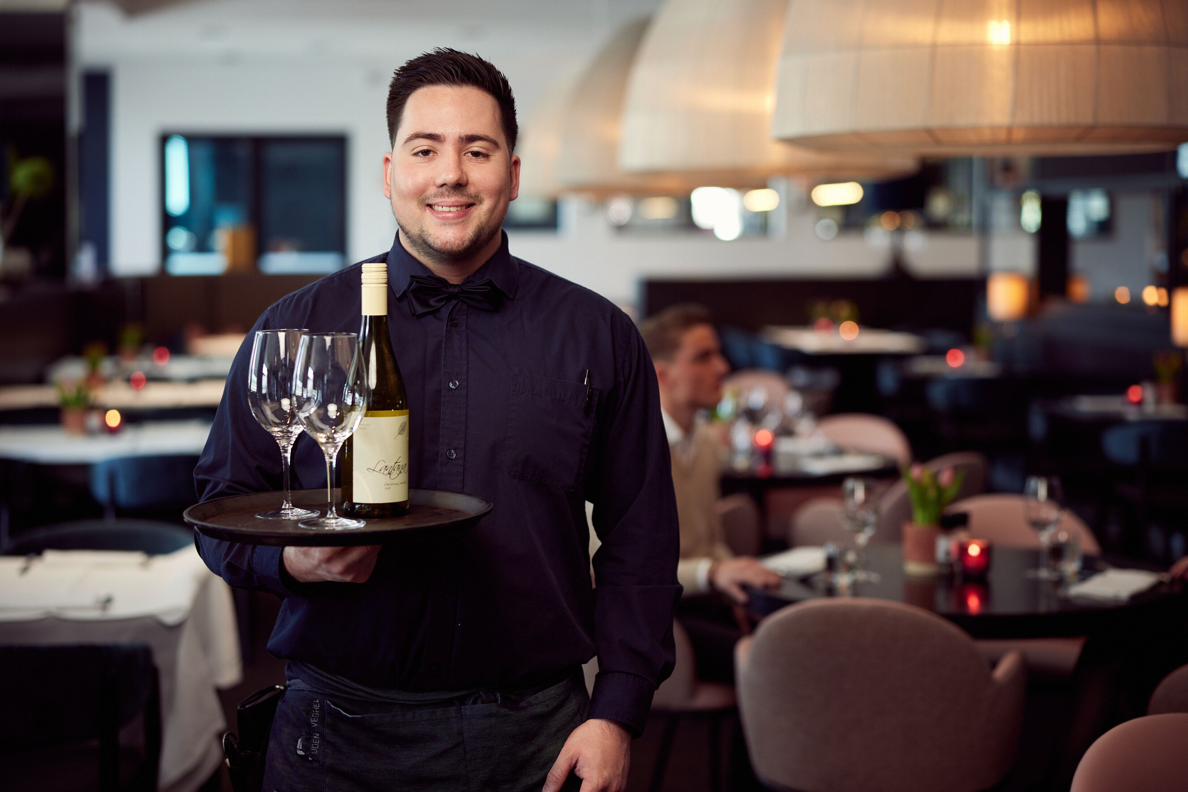 Een ober draagt een dienblad met een fles wijn en glazen in een restaurant.