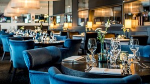 A restaurant with round tables set with wine glasses, plates, and cutlery. There are blue upholstered chairs around the tables. - Van der Valk Hotel Uden-Veghel (Uden)