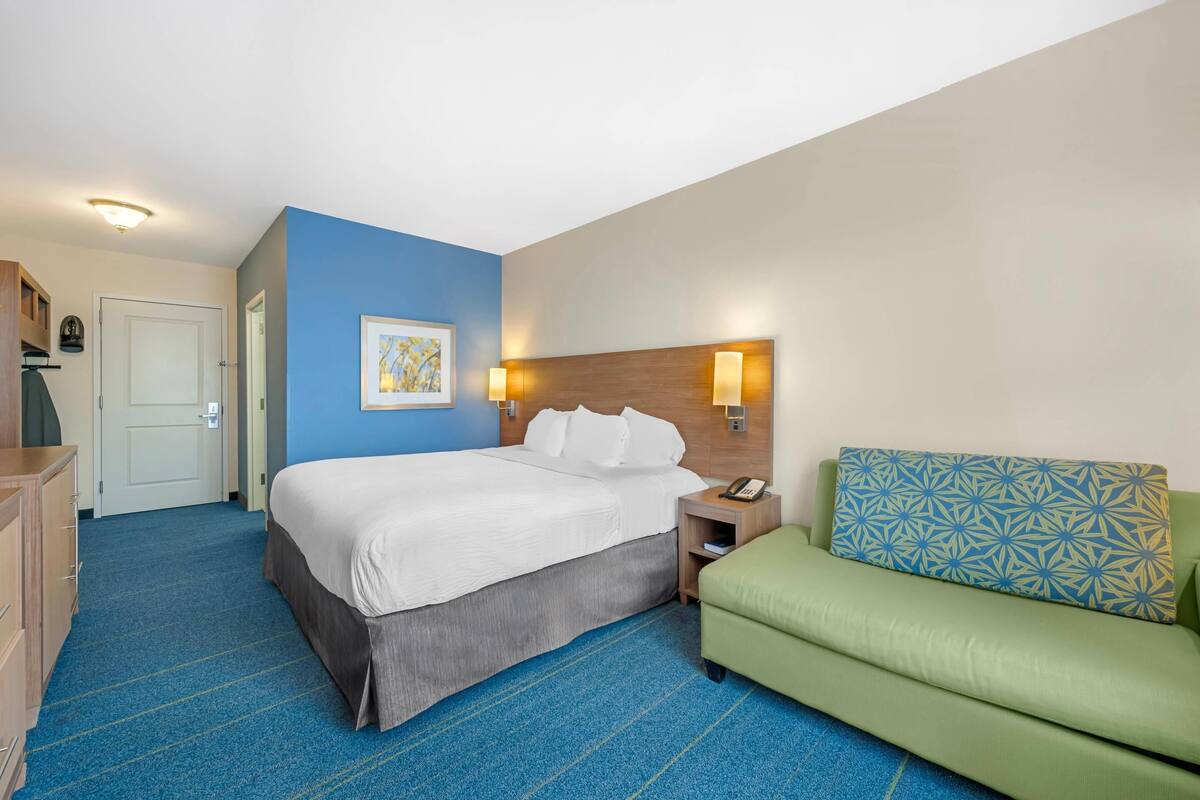 Ein Hotelzimmer mit Bett, Nachttisch, Lampe und einem grünen Sofa.