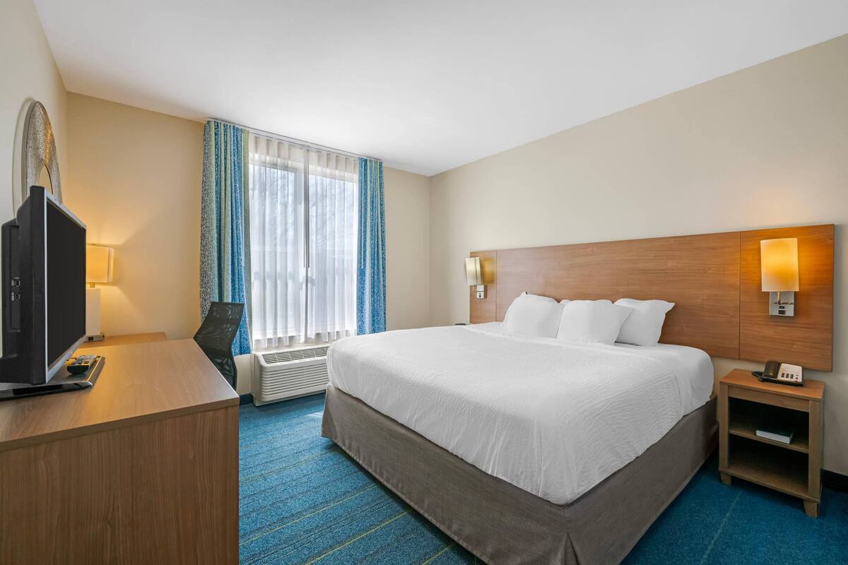 Ein Hotelzimmer mit einem großen Bett, einem Schreibtisch mit Fernseher, einer Lampe und einem Nachttisch mit Telefon.