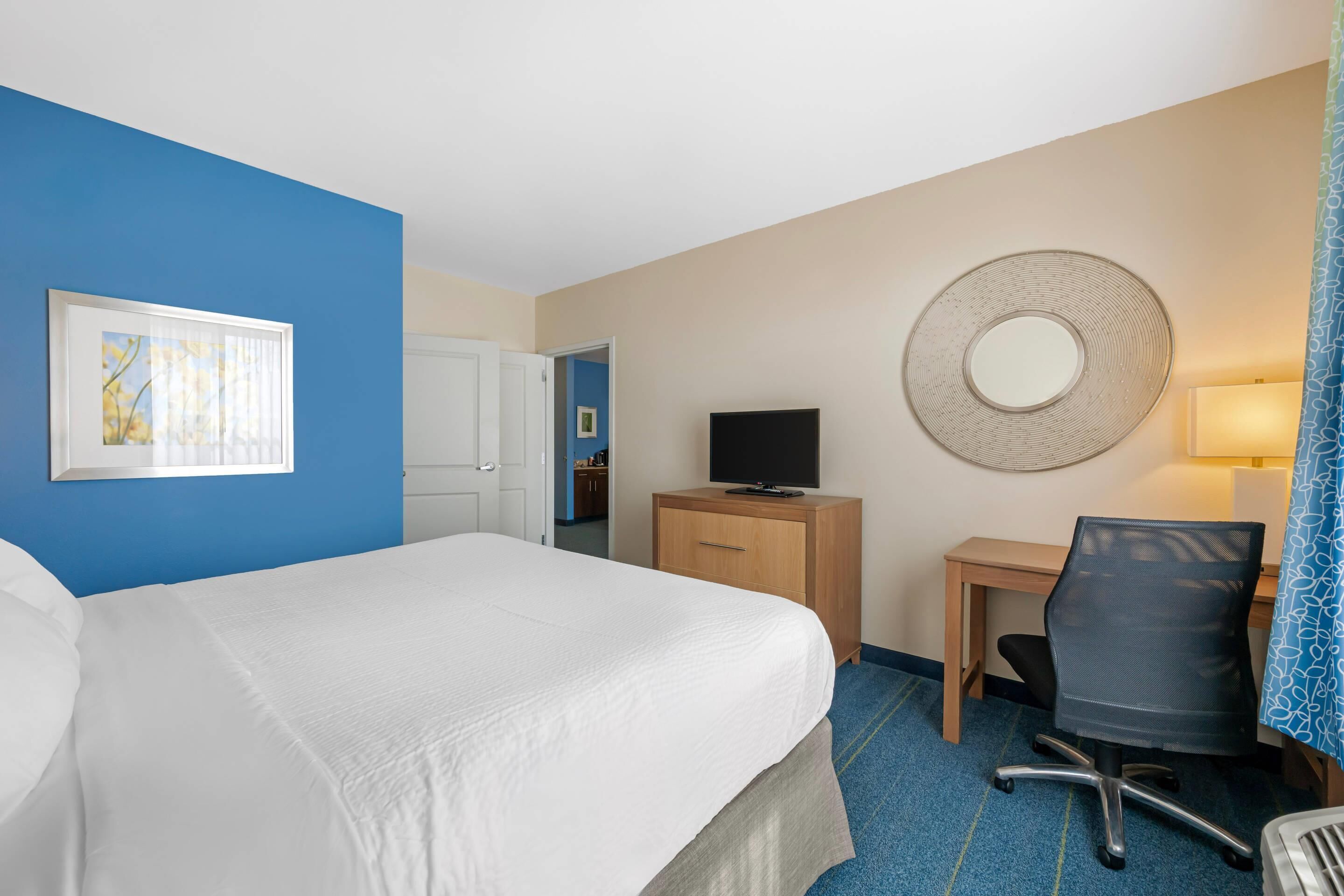 Une chambre d’hôtel équipée d’un lit, d’un bureau, d’une chaise, d’une télévision et d’un miroir fixé au mur.