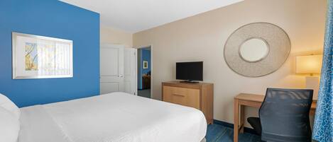 Une chambre d’hôtel équipée d’un lit, d’un bureau, d’une chaise, d’une télévision et d’un miroir fixé au mur.