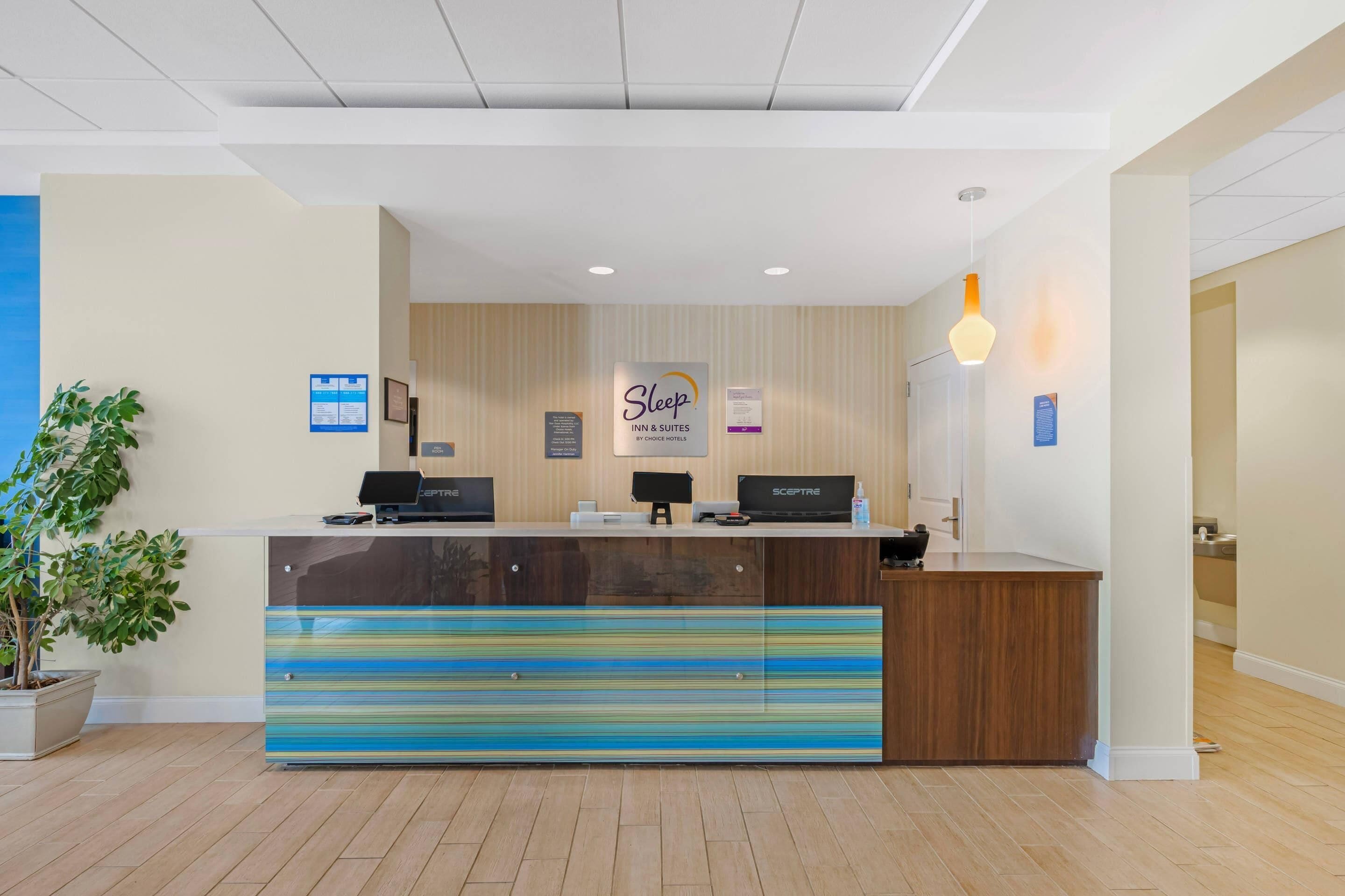 Un mostrador de recepción con diseño a rayas, una planta y un letrero de Sleep Inn & Suites by Choice Hotels.