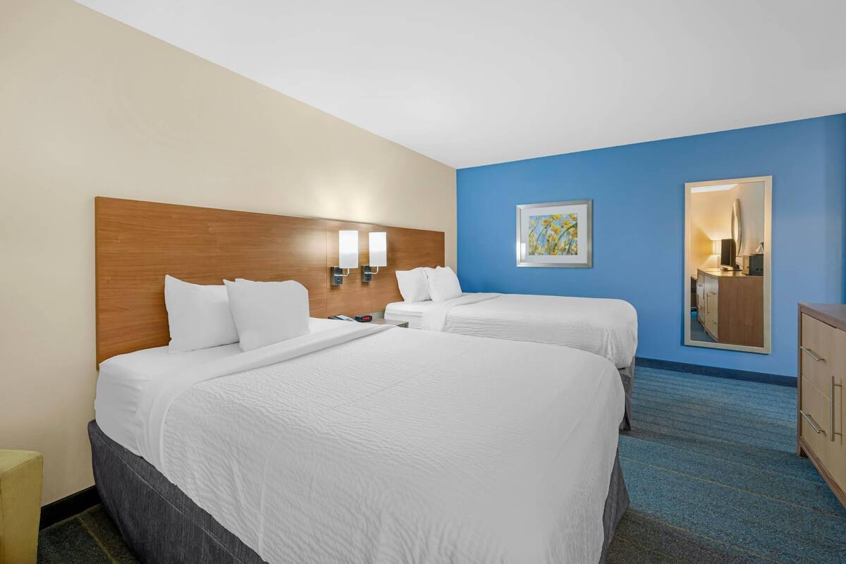 Ein Hotelzimmer mit zwei Betten, einem hölzernen Kopfteil, Wandleuchten, einem gerahmten Bild und einem Spiegel.