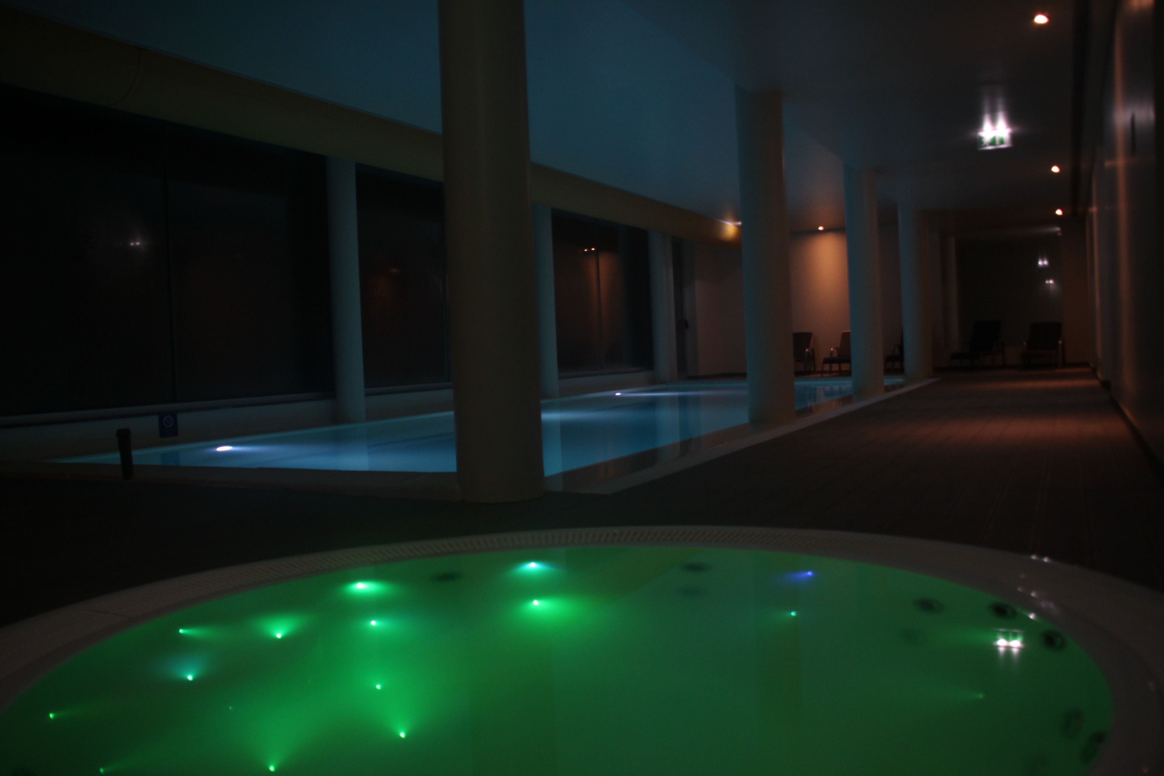 Uma área de piscina interior com iluminação fraca e uma banheira de hidromassagem em primeiro plano.