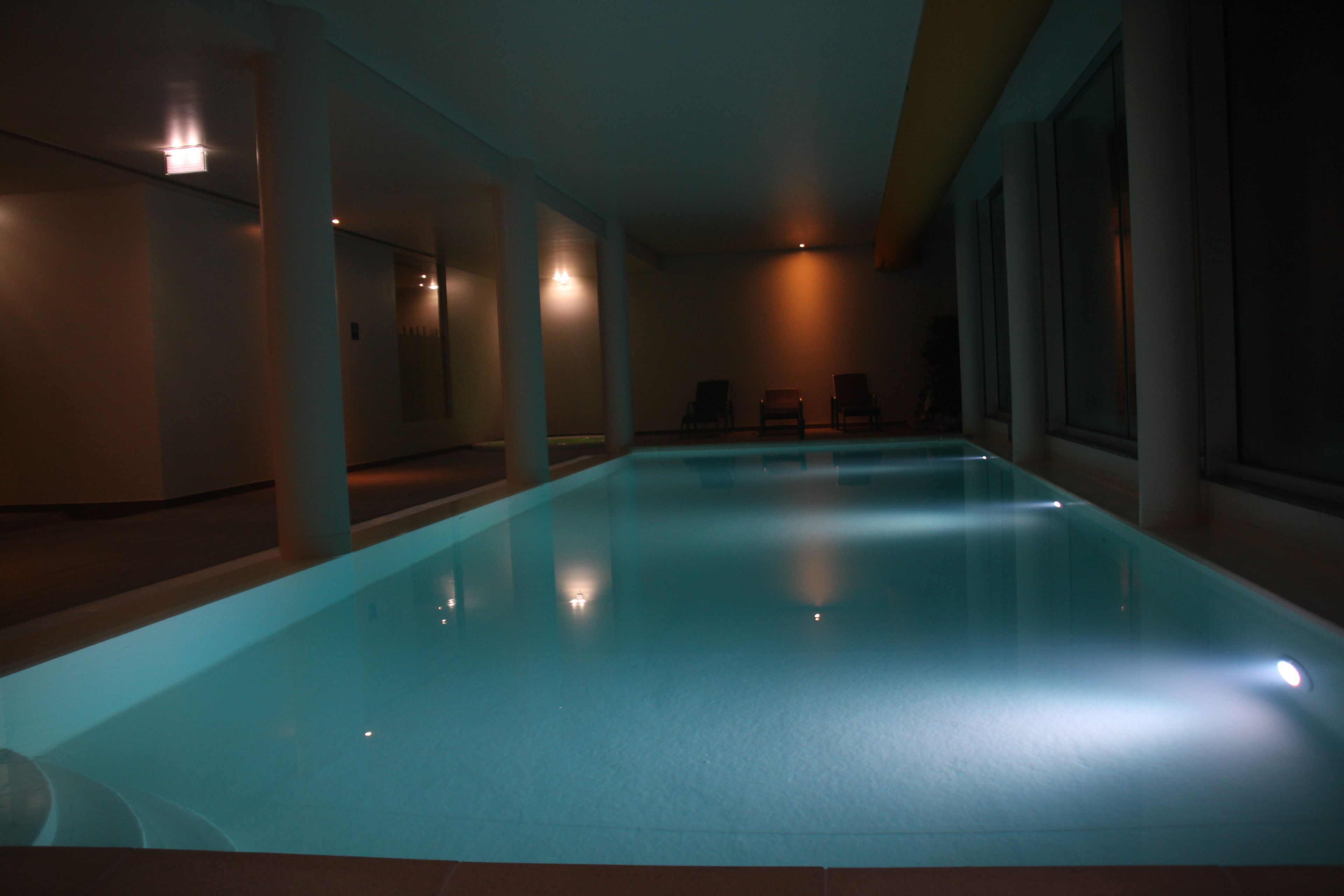 Una piscina interior con agua cristalina, rodeada de paredes y columnas, e iluminada con luz tenue.