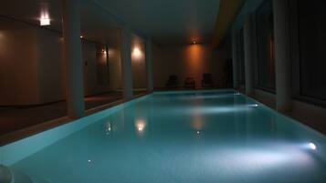 Una piscina interior con agua cristalina, rodeada de paredes y columnas, e iluminada con luz tenue.